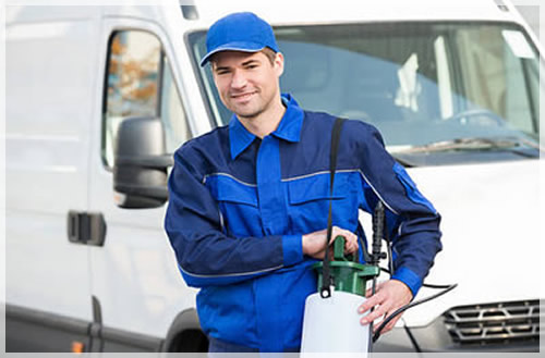 A pest control technician in a blue uniform standing by a service van